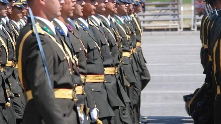 Tören kıyafetli üniformalı personel, açık alanda sıra düzeninde karşılıklı bekliyor.