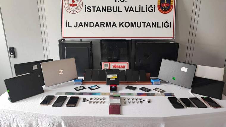 İstanbul İl Jandarma Komutanlığı tabelasının önünde telefon, tablet, bilgisayar ve çeşitli elektronik cihazlar sergileniyor.