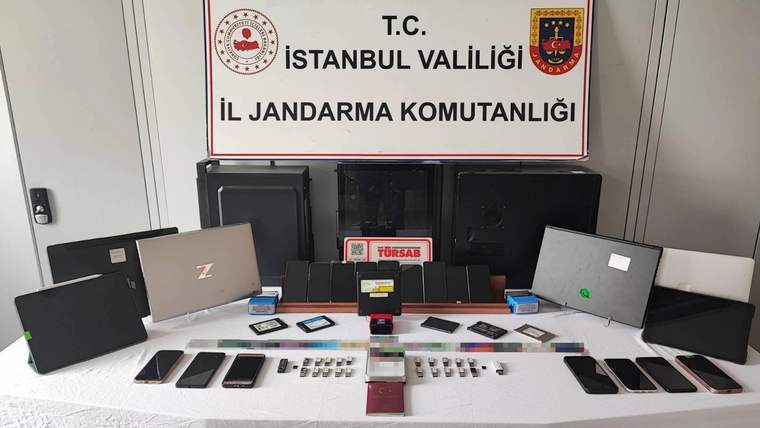 İstanbul İl Jandarma Komutanlığı tabelasının önünde telefon, tablet, bilgisayar ve çeşitli elektronik cihazlar sergileniyor.