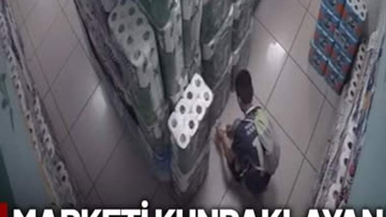 Marketin içinde, tuvalet kağıdı raflarının önünde oturan bir çocuk, yere bir şey bırakıyor.