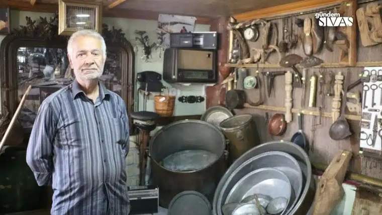 Bir adam, arka planda çeşitli eski eşyaların sergilendiği bir müze odasında duruyor.