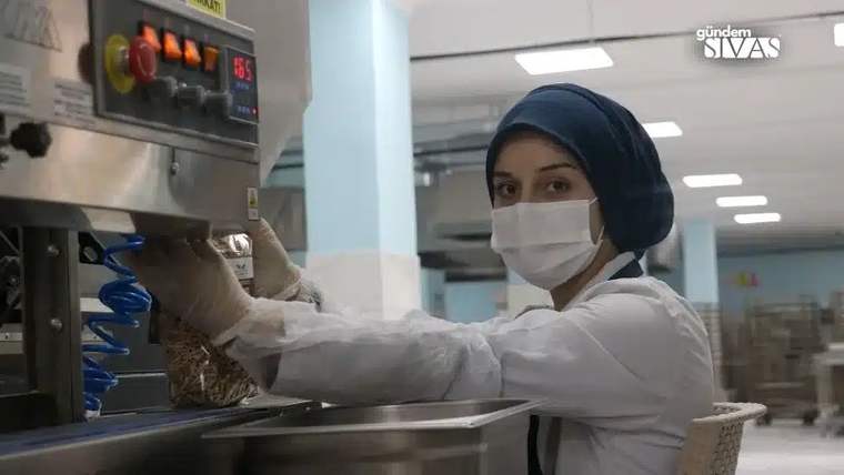 Maske takan bir kadın, mutfak ekipmanını kullanarak üretim yapıyor.