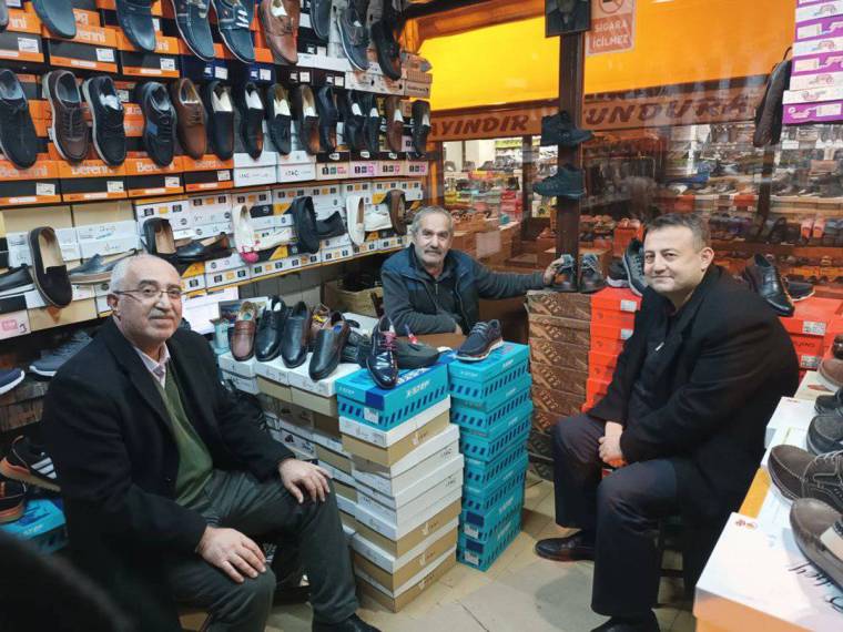Ayakkabı mağazasında raflar ve kutular arasında oturan üç erkek görülüyor.