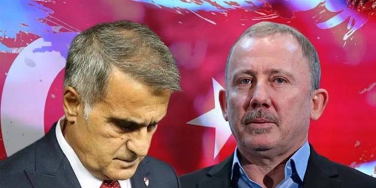 Takım elbiseli iki erkekten biri aşağı bakarken diğeri kameraya bakıyor; arkada Türk bayrağı görülüyor.