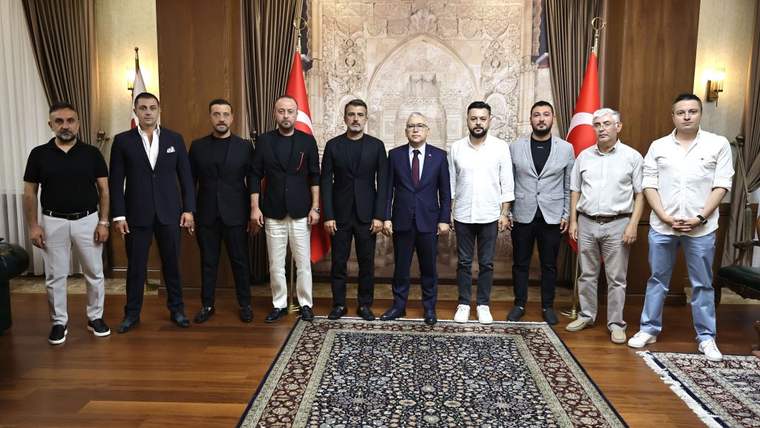 Ahşap panelli bir salonda, Türk bayrakları önünde on kişinin yan yana durduğu görülüyor.