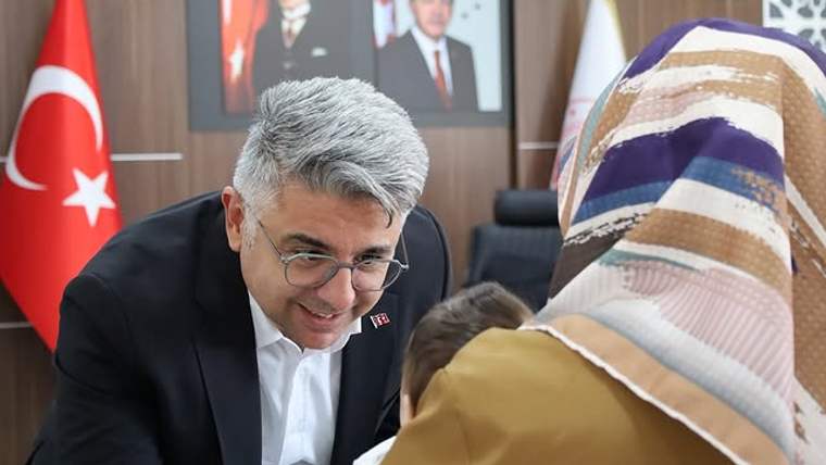 Türk bayrağı ve portrelerin bulunduğu odada bir erkek, başörtülü bir kadınla konuşuyor.