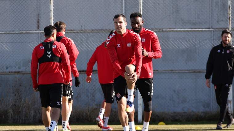 Kırmızı forma giymiş futbolcular, antrenman sahasında ısınma hareketleri yapıyor.