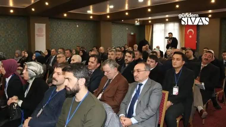 Bir toplantıda oturan kalabalık, bazı katılımcılar ön planda yer alıyor.
