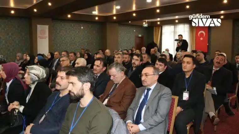 Bir toplantıda oturan kalabalık, bazı katılımcılar ön planda yer alıyor.