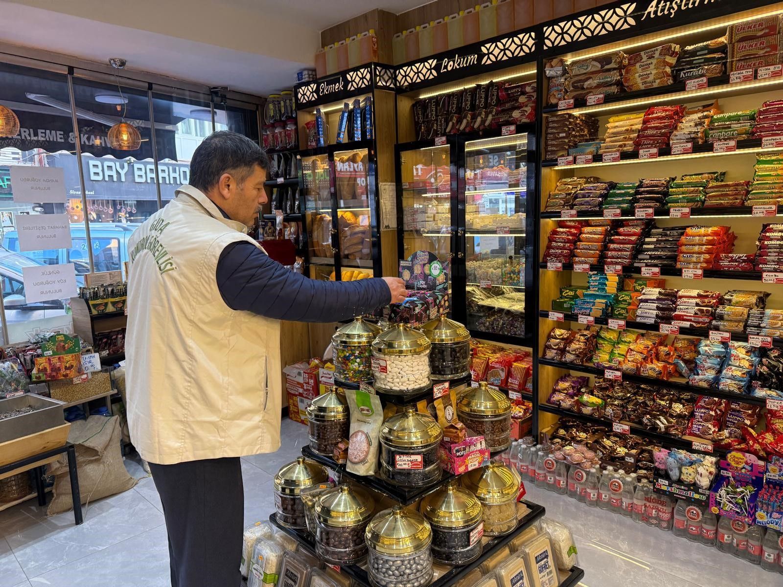Bir gıda denetim görevlisi, marketteki şekerleme ve atıştırmalıkların bulunduğu rafları inceliyor.