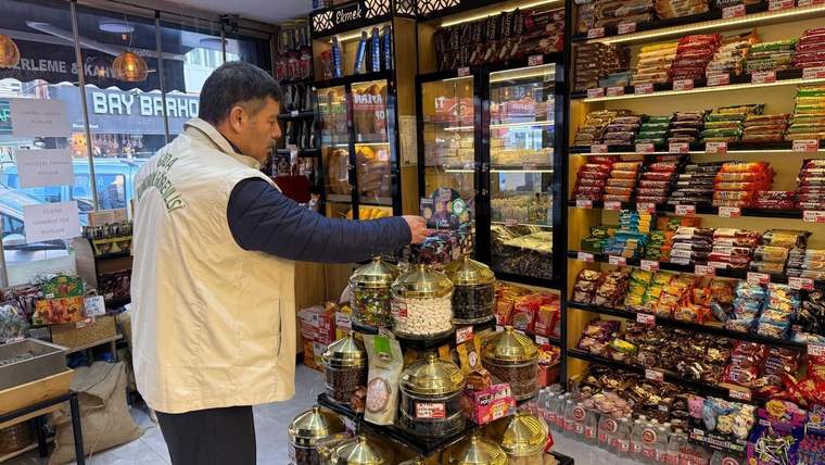 Bir gıda denetim görevlisi, marketteki şekerleme ve atıştırmalıkların bulunduğu rafları inceliyor.