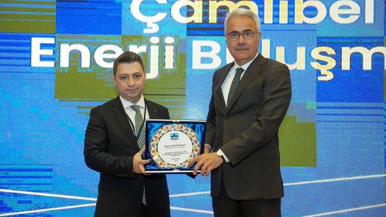 Bir kişi ödül alırken diğer kişiyle el sıkışıyor, arka planda "Çamlıbel Enerji Buluşması" yazılı ekran var.