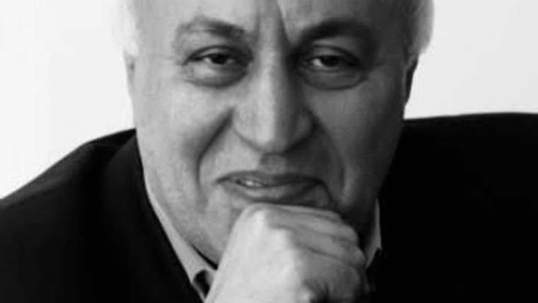 Siyah beyaz portrede, takım elbiseli bir adam elini çenesine dayamış, kameraya doğru bakıyor.