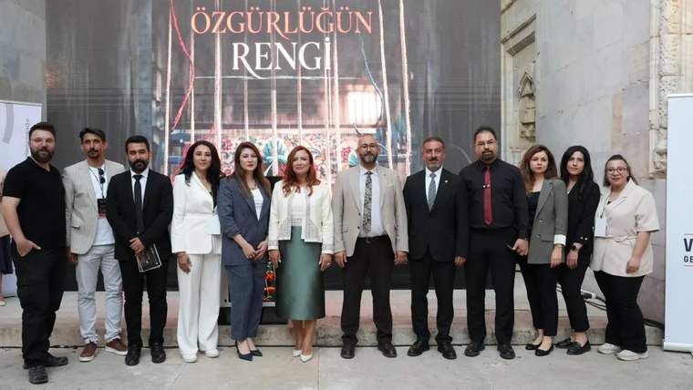Bir grup insan, "Özgürlüğün Rengi" yazılı arka planda poz veriyor.