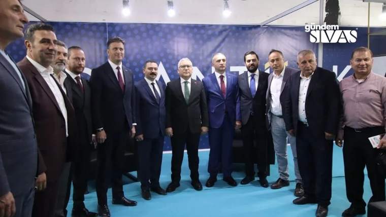 Kapalı bir salonda takım elbiseli ve günlük giyimli bir grup erkek yan yana poz veriyor.