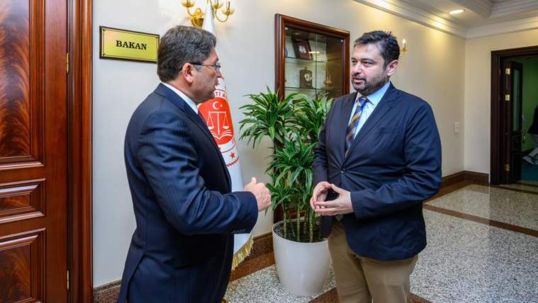 Kapısında “BAKAN” yazan odanın önünde iki takım elbiseli erkek, bitkinin yanında konuşuyor.