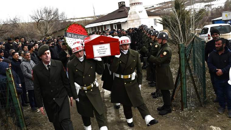 Askeri kıyafet giymiş askerler, tabutun etrafında yürüyerek kalabalığın önünden geçiyor.
