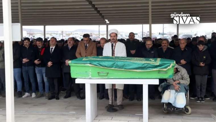 Yeşil örtüyle kaplı bir tabutun çevresinde, kapalı alanda çok sayıda kişi bekliyor.