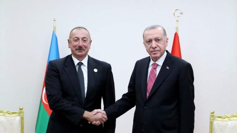 İki erkek, Azerbaycan ve Türkiye bayrakları önünde takım elbiseleriyle el sıkışıyor.
