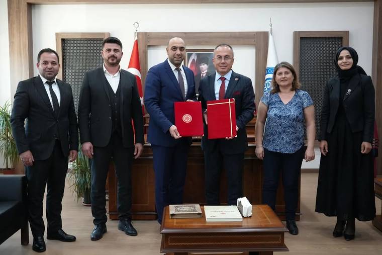 Bir odada altı kişi yan yana duruyor; ortadaki iki kişi kırmızı dosyalar tutarken arkada Türk bayrağı görülüyor.