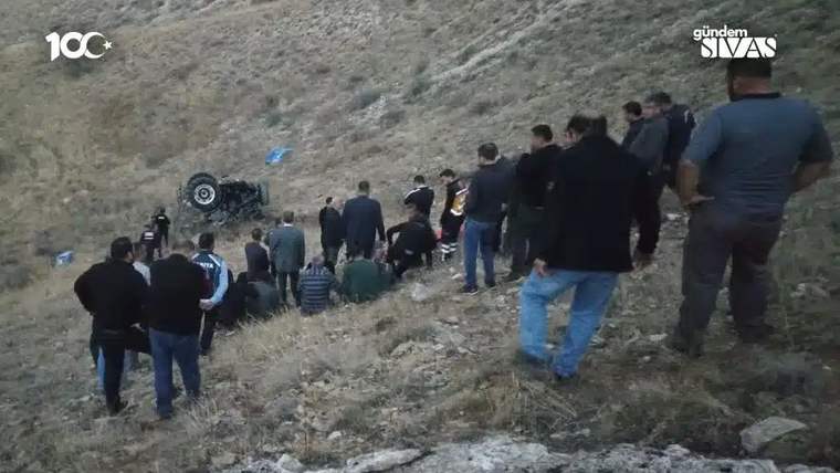 Bir grup insan, uçurumun kenarında devrilmiş bir traktörü inceliyor.