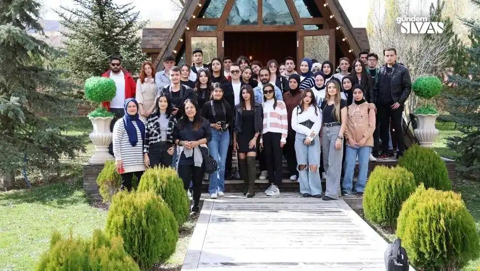 Bir grup genç, bir ahşap yapının önünde poz veriyor; arka planda ağaçlar ve çalılar var.