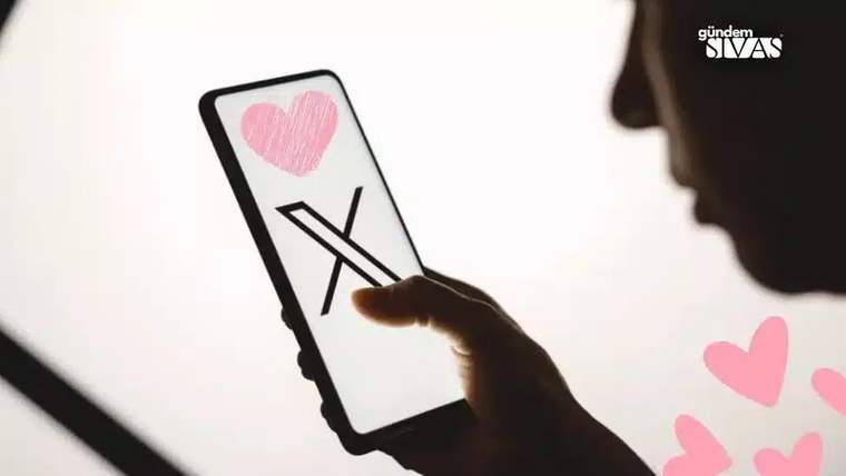 Ekranında pembe kalp ve X işareti bulunan akıllı telefon, bir el tarafından tutuluyor; yanında kalp şekilleri görülüyor.