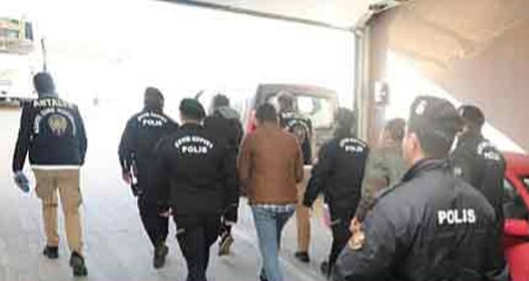 Üzerlerinde polis yazılı montlar bulunan görevliler, bir kişiyi bina içindeki koridorda götürüyor.