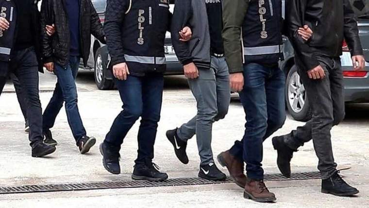 Üzerlerinde “POLİS” yazılı yelekler bulunan görevliler, birkaç erkeğin yanında bir araç önünde yürüyor.