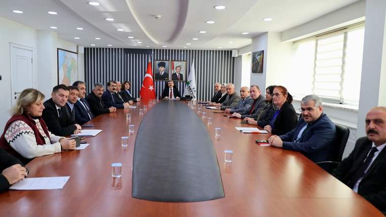 Uzun toplantı masası çevresinde oturan kişiler, Türk bayrağı ve çeşitli flamaların bulunduğu salonda görüşüyor.