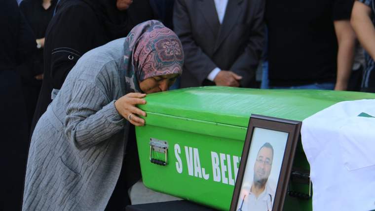 Bir kadın, üzerinde "SIVAS BELE..." yazılı yeşil tabutun başında dururken yanında portreli çerçeve görülüyor.