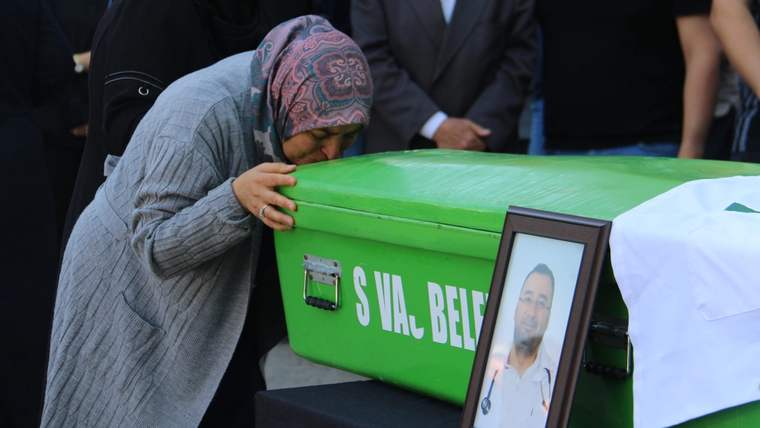 Bir kadın, üzerinde "SIVAS BELE..." yazılı yeşil tabutun başında dururken yanında portreli çerçeve görülüyor.