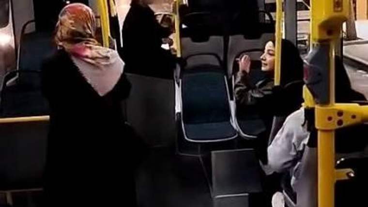 Bir otobüsün içinde, iki kadın arasında tartışma yaşanıyor; diğer yolcular ise izliyor.