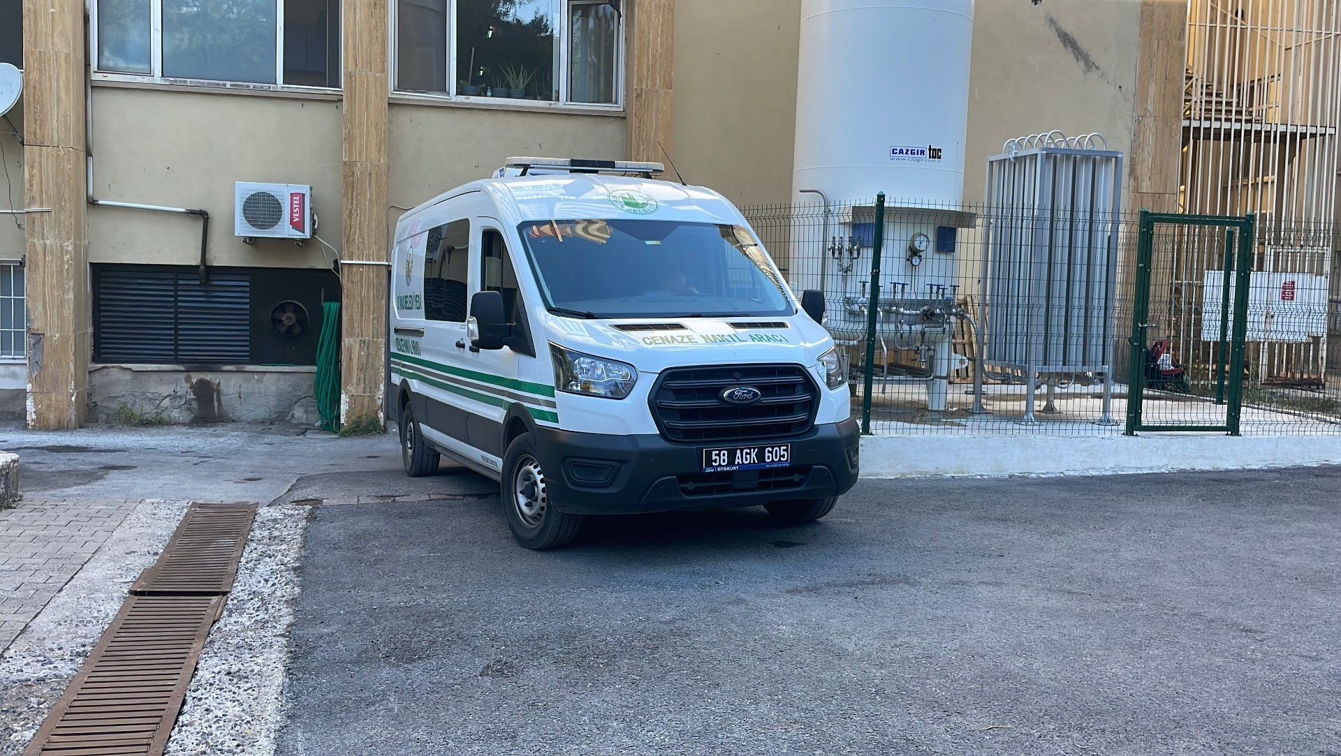 Yeşil şeritli bir ambulans, bir binanın önündeki asfalt alanda park halinde duruyor.