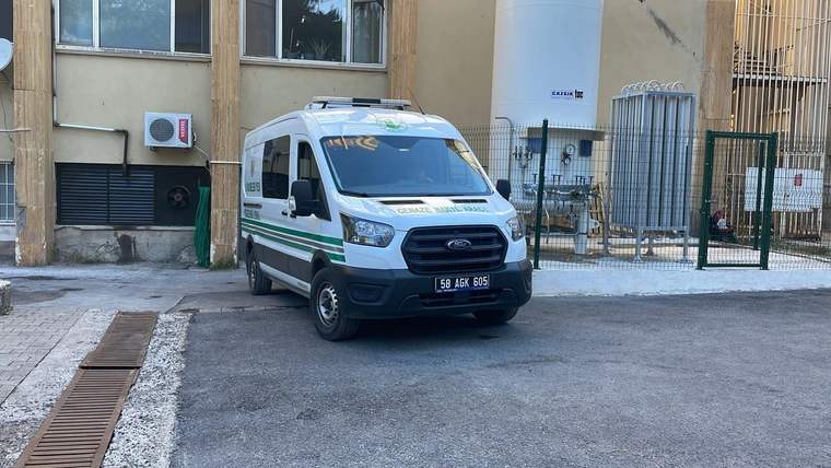 Yeşil şeritli bir ambulans, bir binanın önündeki asfalt alanda park halinde duruyor.