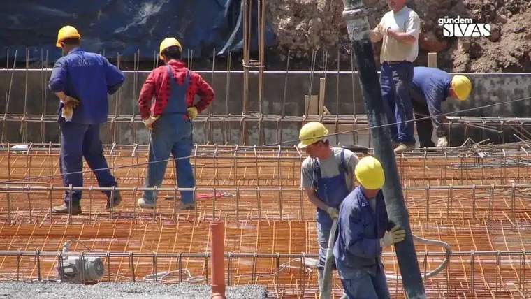 Şantiye alanında çalışan işçiler, inşaat demirleri ve beton pompası ile birlikte görünüyor.