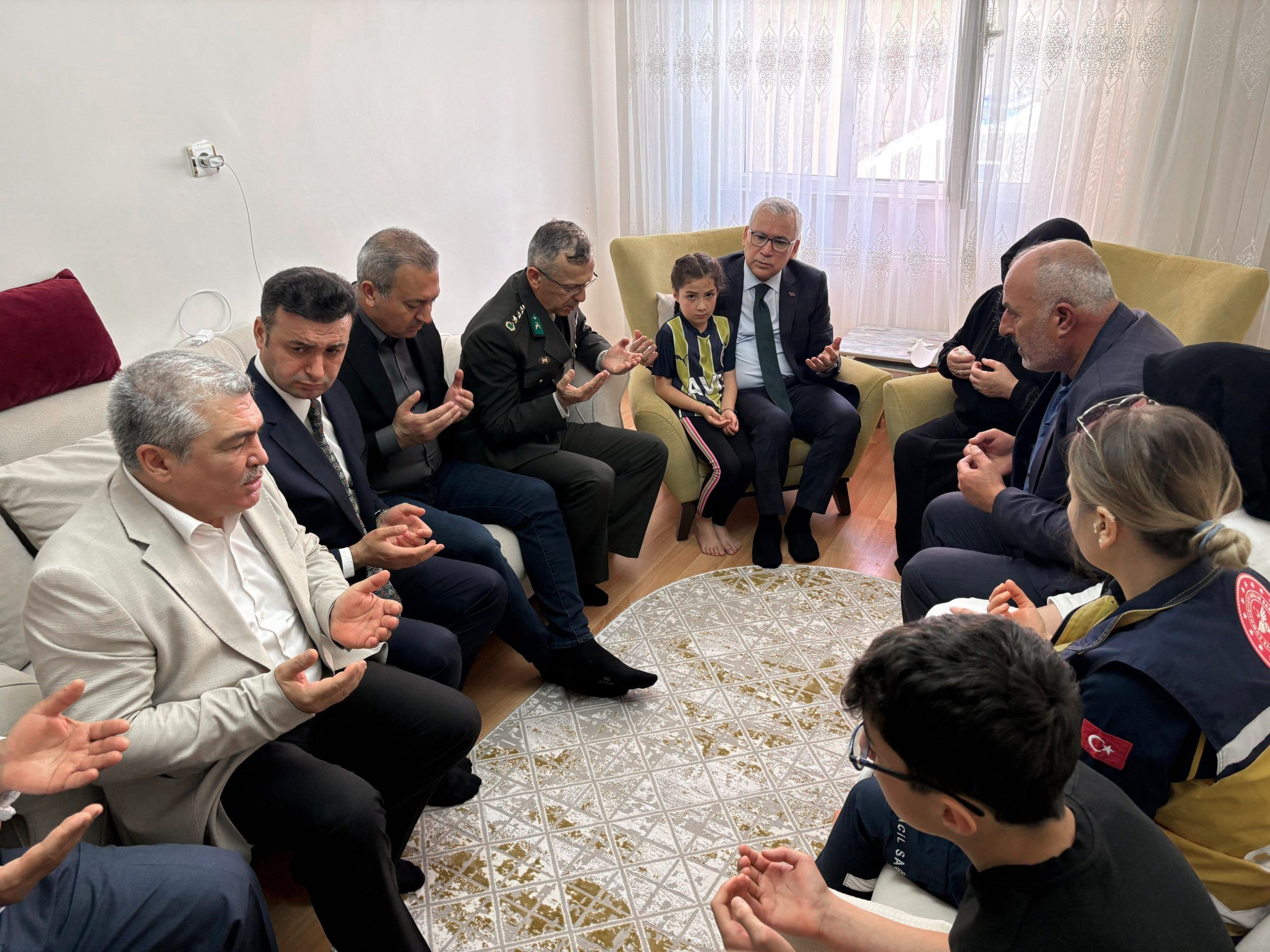 Bir grup insan, oturma odasında dua ediyor; bazıları çocukla birlikte oturuyor.