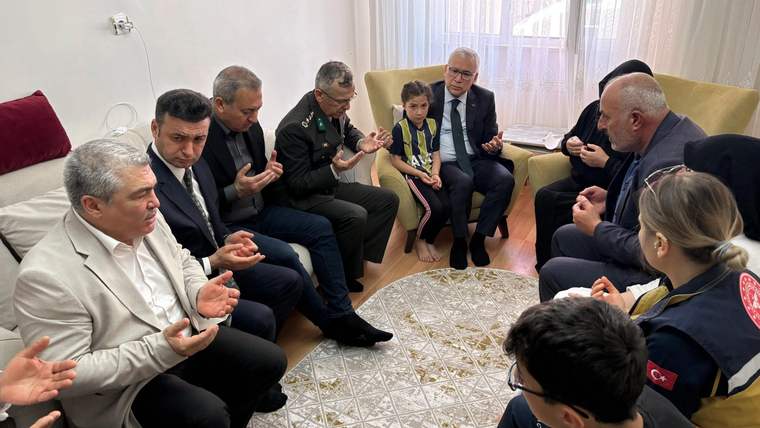 Bir grup insan, oturma odasında dua ediyor; bazıları çocukla birlikte oturuyor.