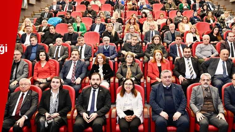 Kırmızı koltuklu salonda çok sayıda kişi oturuyor; soldaki kırmızı panelde etkinlik bilgileri yer alıyor.