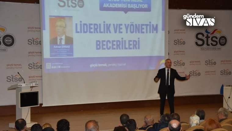 Sahnede konuşan bir kişi, arkasındaki perdede “Liderlik ve Yönetim Becerileri” yazılı sunum önünde duruyor.