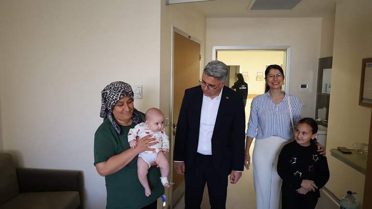 Bir kadın kucağında bebek tutarken, yanında üç kişi duruyor; bir adam, bir kadın ve bir kız çocuğu.