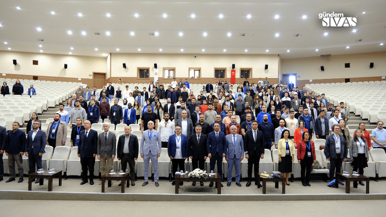 Konferansa katılan kalabalık bir grup, sahnede sıraya dizilmiş şekilde duruyor.