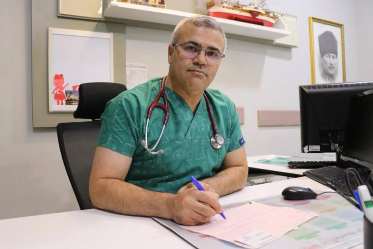 Yeşil önlük giymiş bir doktor, masasında oturarak not alıyor.