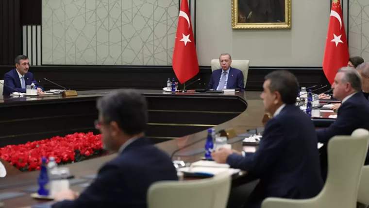 Bir toplantı odasında, masanın etrafında oturan beş kişi ve arka planda Türk bayrakları ile bir portre görünmekte.