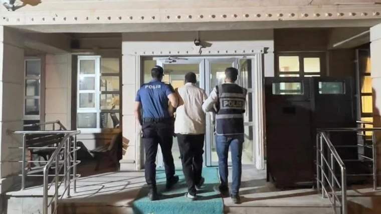 İki polis memuru, bir kişiyi bina girişine doğru götürüyor.