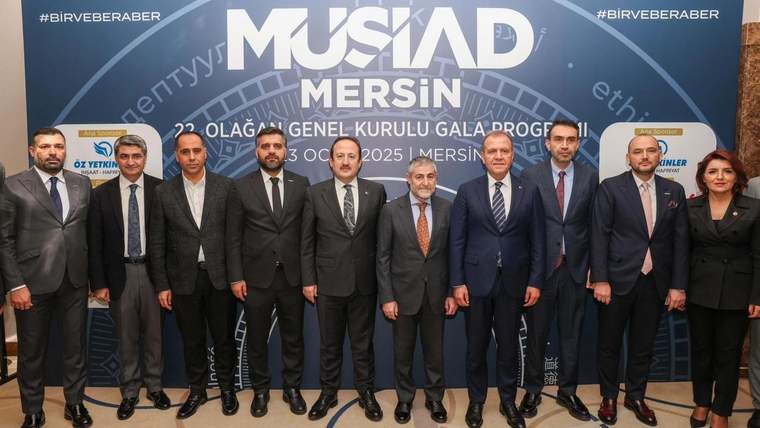 MÜSİAD Mersin yazılı afiş önünde, takım elbiseli dokuz erkek ve bir kadın yan yana duruyor.