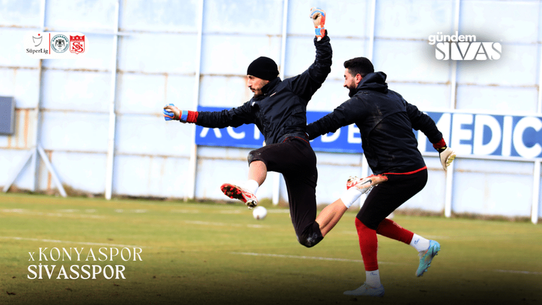 Antrenman sahasında kaleci, topa zıplayarak vuruyor; arkada bir oyuncu koşuyor.