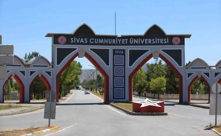Sivas Cumhuriyet Üniversitesi yazılı giriş takı, kampüs yolunun üzerinde ve ağaçların arasında görülüyor.