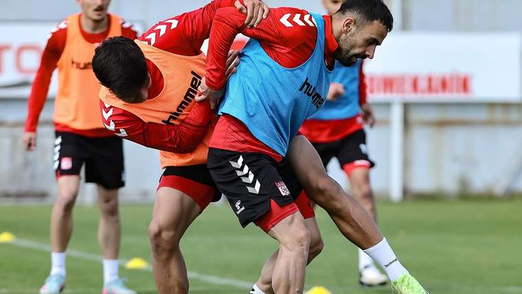 Antrenman sahasında, futbolcular birbirleriyle mücadele ediyor. İki oyuncu, antrenman yelekleri giymekte.