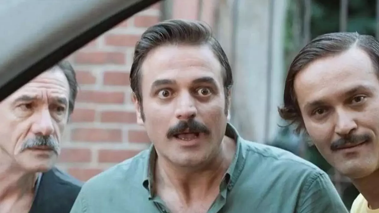 Üç erkeğin bir arada bulunduğu bir sahne, biri şaşkın bir ifadeyle bakıyor.